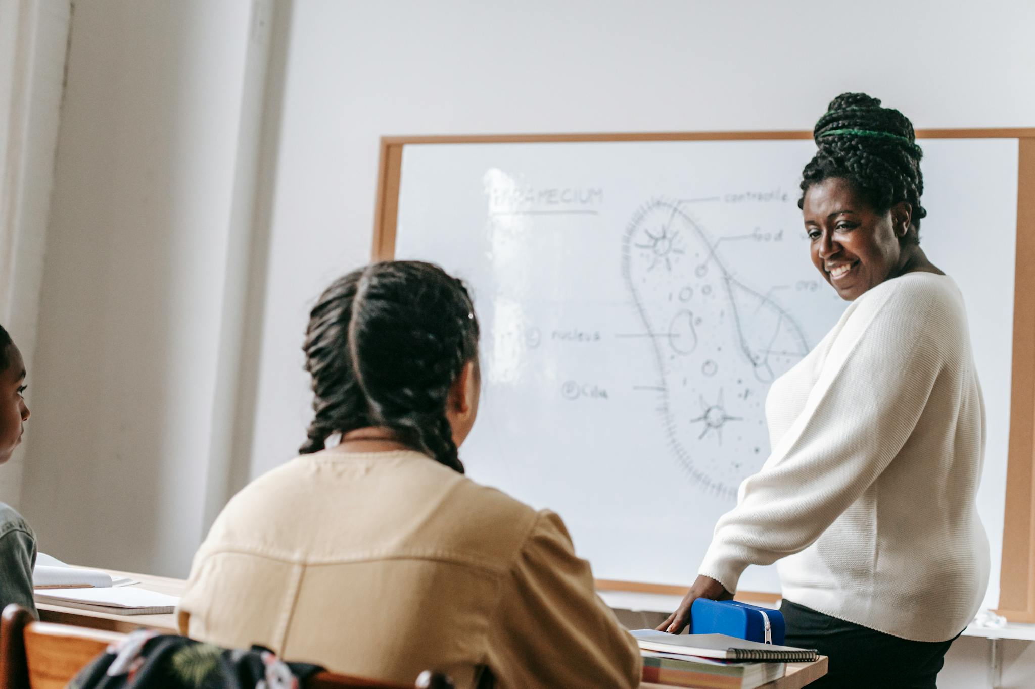 A biology teacher smiles while teaching students a science lesson in a classroom setting.