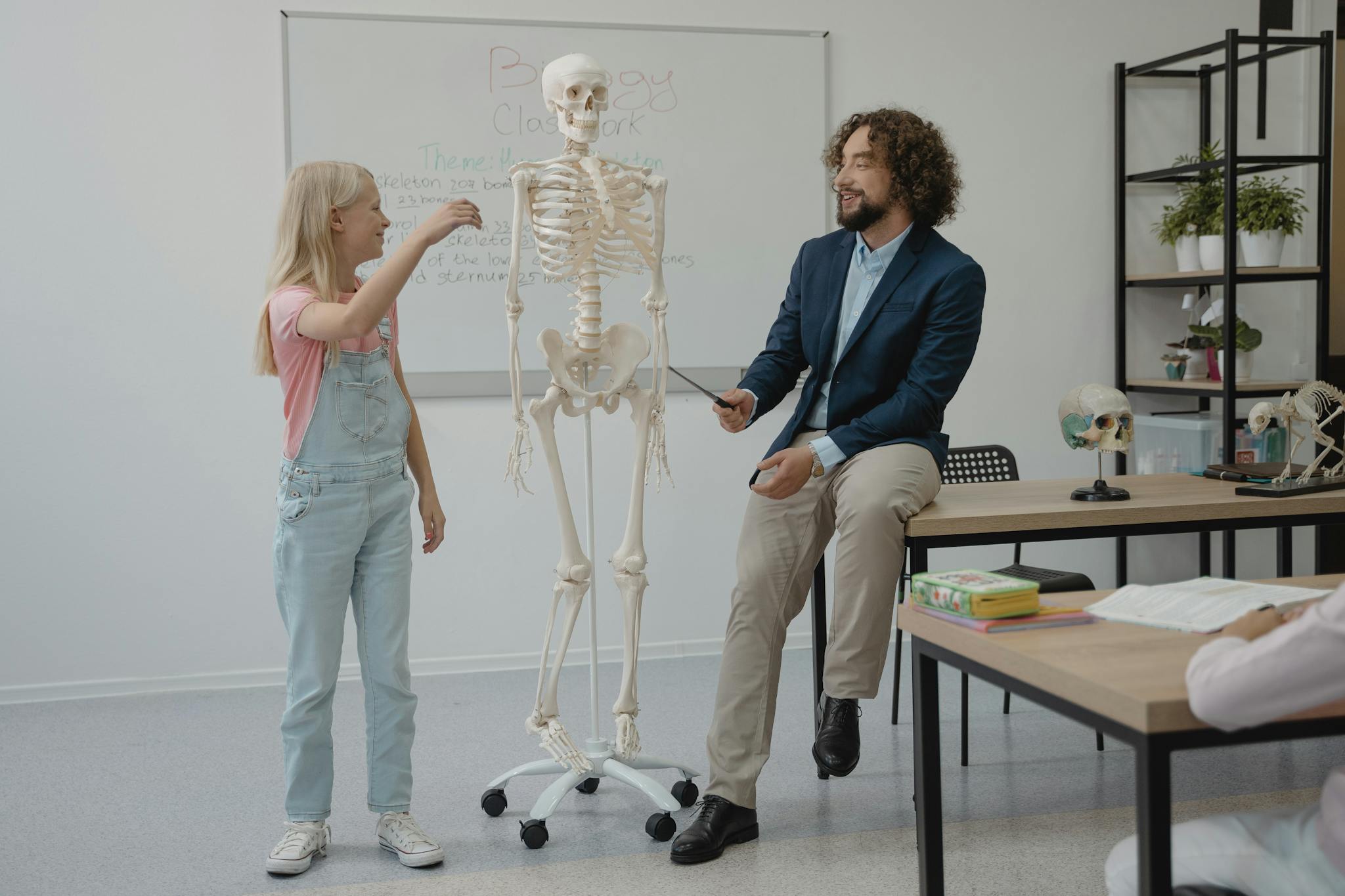 Home 1 Teacher and student interact with a skeleton model during a lively biology lesson in a classroom.